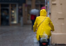 One unrecognizable person with yellow oilskin on bike riding through rainy street in old narrow shooping street with cobblestones on rainy day