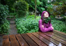 Beautiful young woman enjoying the rain in a garden decorated with eyes closed sits wooden table