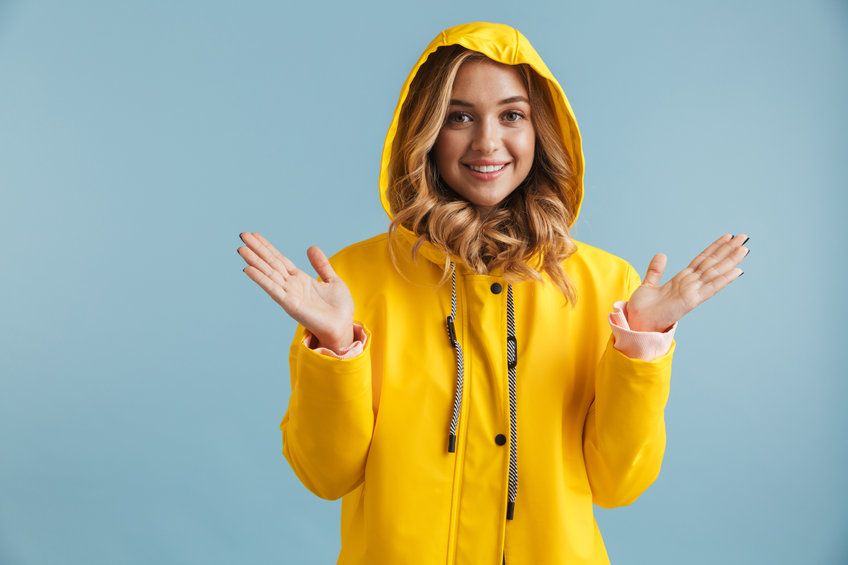 Image of joyful woman 20s wearing yellow raincoat looking at camera isolated over blue background