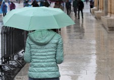 A woman with green jacket and green umbrella walks in the rain